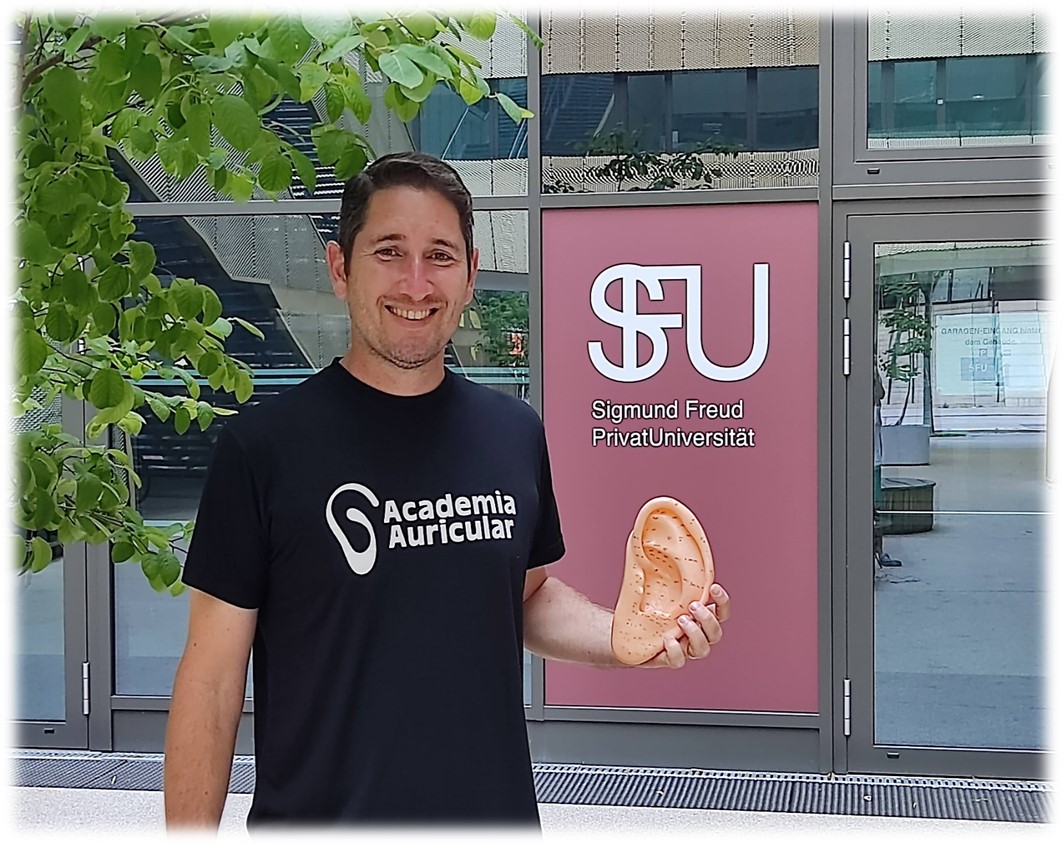 Marcos Martini diante da Sigmund Freud PrivatUniversität, em Viena, segurando um modelo de orelha